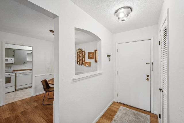 foyer entrance featuring a textured ceiling, baseboards, and wood finished floors