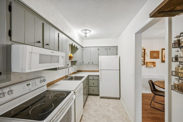 kitchen featuring white appliances, light countertops, a textured ceiling, gray cabinetry, and a sink