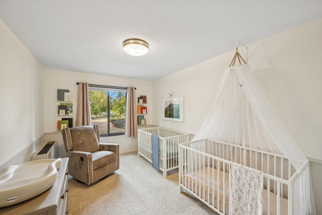 bedroom featuring a crib, radiator heating unit, a textured ceiling, and light colored carpet