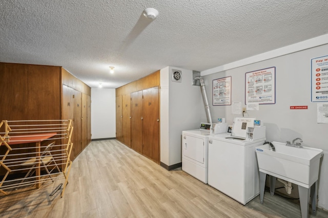 common laundry area featuring light wood-type flooring, baseboards, washer and clothes dryer, and a textured ceiling