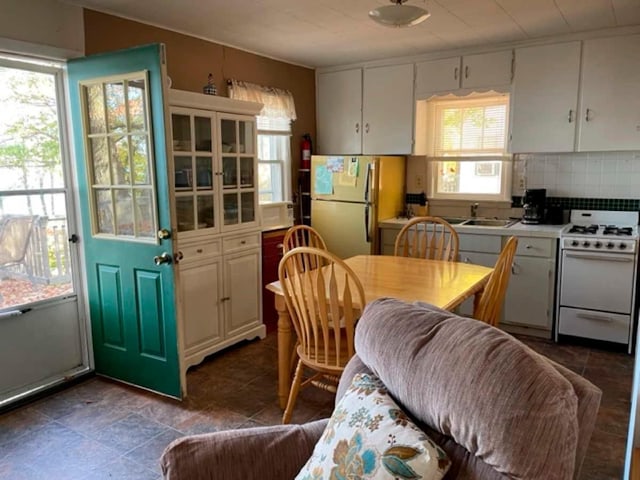 kitchen with fridge, white range with gas stovetop, white cabinets, and decorative backsplash