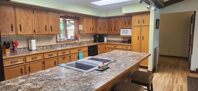 kitchen featuring stovetop, sink, a breakfast bar area, dishwasher, and white microwave