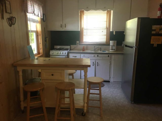 kitchen featuring a breakfast bar, white cabinetry, white gas range, sink, and stainless steel fridge