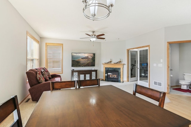 dining room with ceiling fan with notable chandelier, a high end fireplace, and wood-type flooring