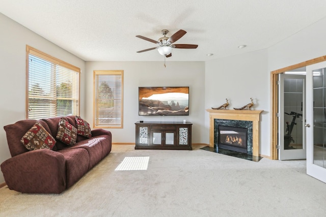 living room featuring ceiling fan, carpet, a high end fireplace, a textured ceiling, and french doors