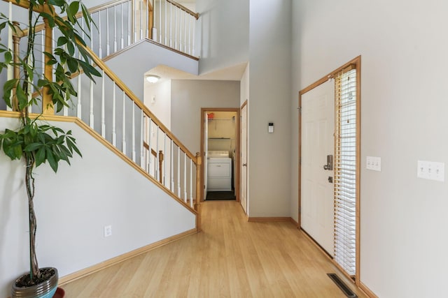 foyer entrance featuring washer / dryer, a towering ceiling, and light wood-type flooring