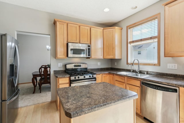 kitchen with appliances with stainless steel finishes, light brown cabinetry, sink, a center island, and light hardwood / wood-style flooring