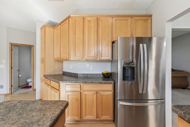 kitchen featuring stainless steel refrigerator with ice dispenser, dark stone counters, and a textured ceiling