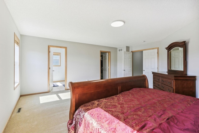 bedroom with ensuite bath, light carpet, and a textured ceiling