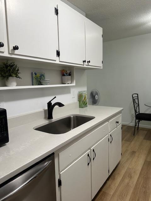 kitchen with sink, stainless steel dishwasher, light hardwood / wood-style floors, and white cabinetry