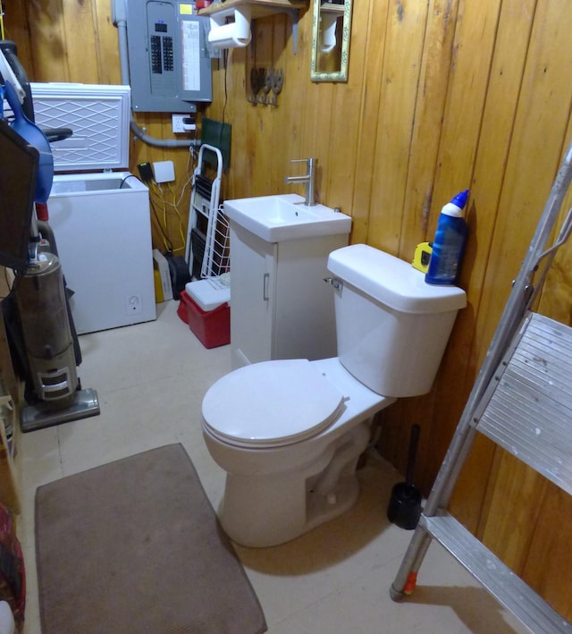 bathroom featuring wooden walls, vanity, toilet, and electric panel