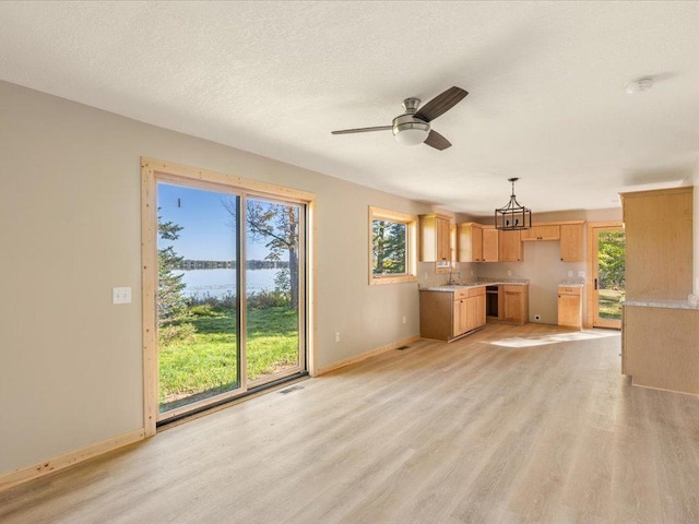 unfurnished living room featuring a water view, a sink, light wood-type flooring, baseboards, and ceiling fan with notable chandelier
