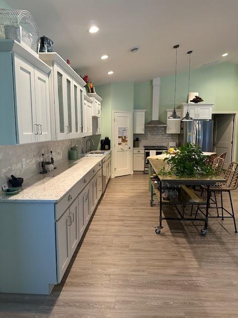 kitchen with pendant lighting, light hardwood / wood-style floors, white cabinetry, wall chimney exhaust hood, and stainless steel appliances