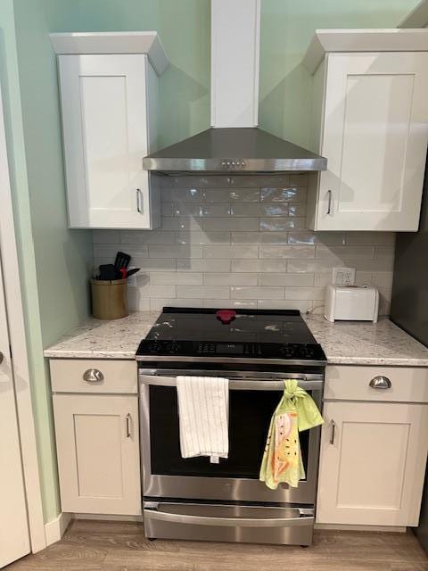 kitchen featuring light wood-type flooring, white cabinetry, stainless steel range, and wall chimney range hood