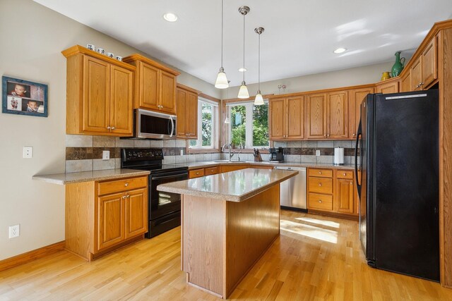 kitchen with light wood-type flooring, black appliances, a kitchen island, and hanging light fixtures