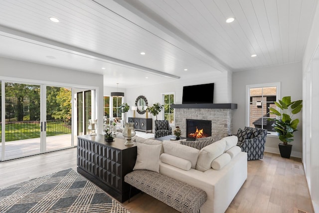 living room with light hardwood / wood-style flooring, beamed ceiling, and a stone fireplace