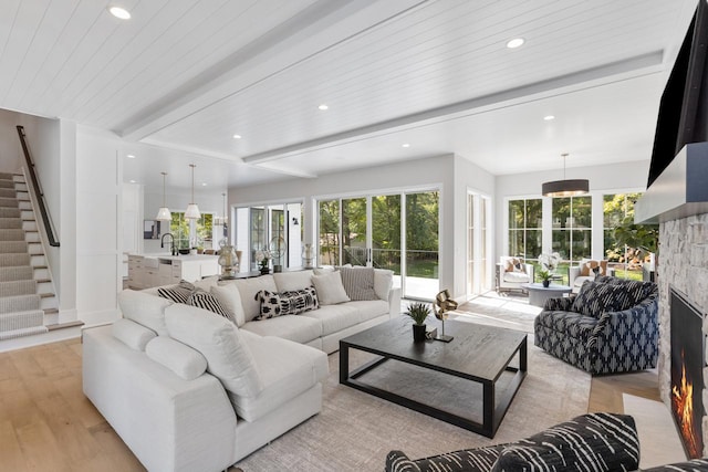 living room with light hardwood / wood-style flooring, beam ceiling, wooden ceiling, and a stone fireplace