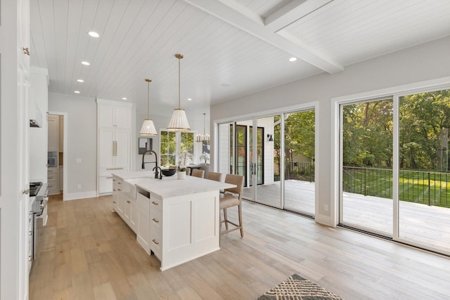 kitchen with hanging light fixtures, light hardwood / wood-style floors, white cabinetry, an island with sink, and beam ceiling