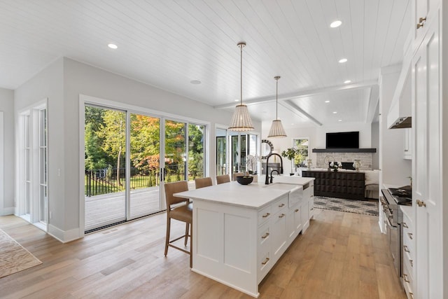 kitchen with light hardwood / wood-style flooring, white cabinets, a center island with sink, and hanging light fixtures