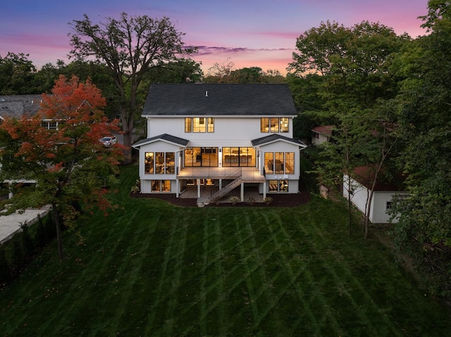 back house at dusk featuring a lawn