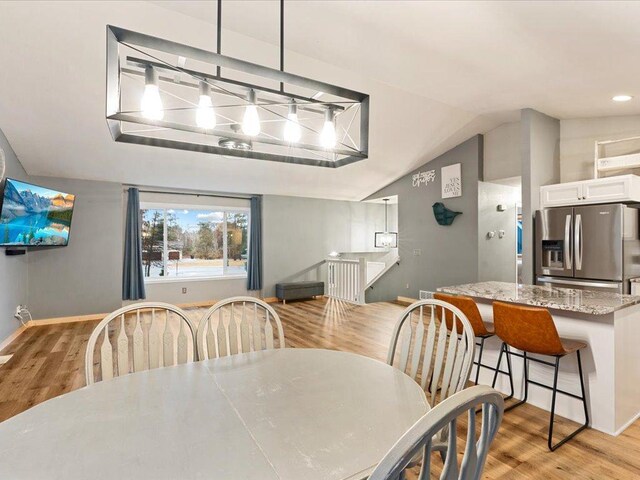 dining area featuring light wood finished floors, baseboards, and vaulted ceiling