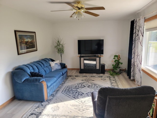 living room with ceiling fan, a multi sided fireplace, light hardwood / wood-style floors, and a healthy amount of sunlight