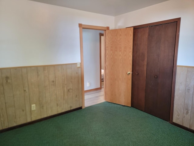 unfurnished bedroom featuring carpet flooring, wood walls, and a closet