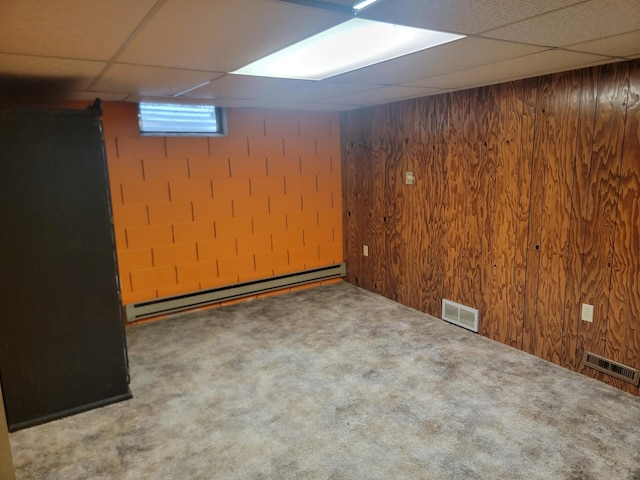 basement with carpet floors, a paneled ceiling, wood walls, and a baseboard heating unit