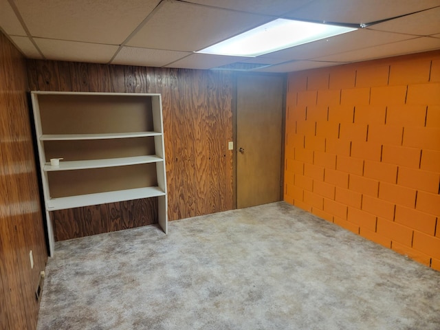 basement with wood walls, carpet flooring, and a paneled ceiling