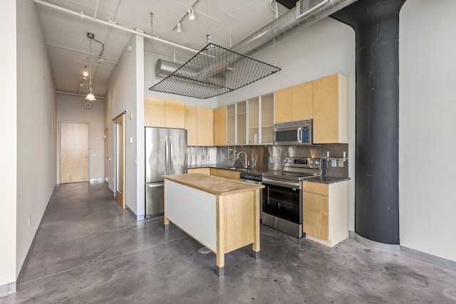 kitchen with appliances with stainless steel finishes, butcher block countertops, a kitchen island, a high ceiling, and light brown cabinetry