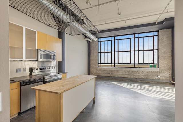 kitchen with appliances with stainless steel finishes, brick wall, light brown cabinets, wooden counters, and a center island