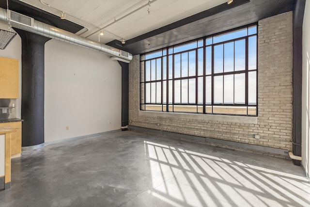 spare room featuring a wealth of natural light, concrete flooring, and brick wall