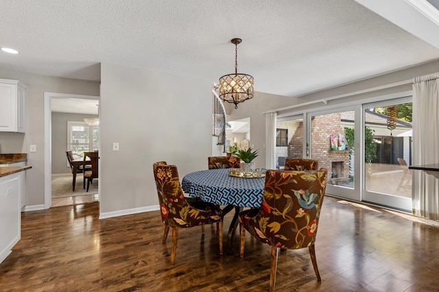 dining area with a chandelier, a brick fireplace, a textured ceiling, and dark hardwood / wood-style flooring