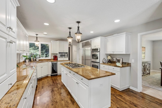 kitchen with white cabinets, light stone counters, dark wood-type flooring, built in appliances, and a center island