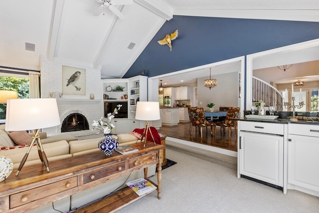 living room featuring beam ceiling, light hardwood / wood-style flooring, a brick fireplace, high vaulted ceiling, and ceiling fan with notable chandelier