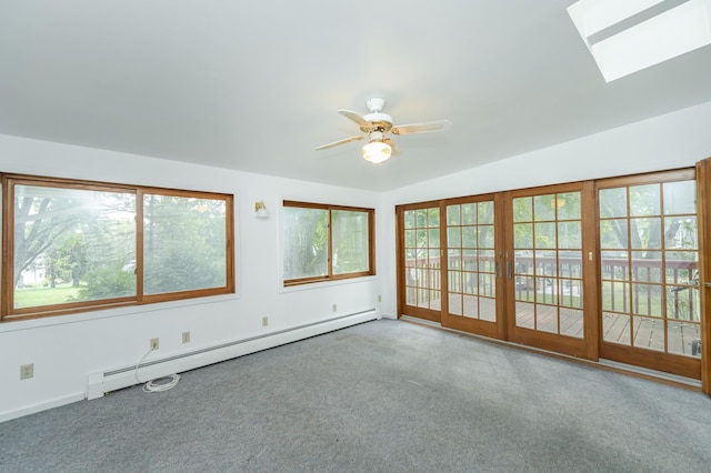 empty room featuring a healthy amount of sunlight, vaulted ceiling with skylight, ceiling fan, and a baseboard heating unit