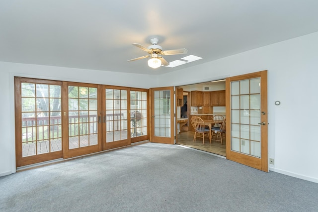 unfurnished living room with a skylight, ceiling fan, and carpet floors