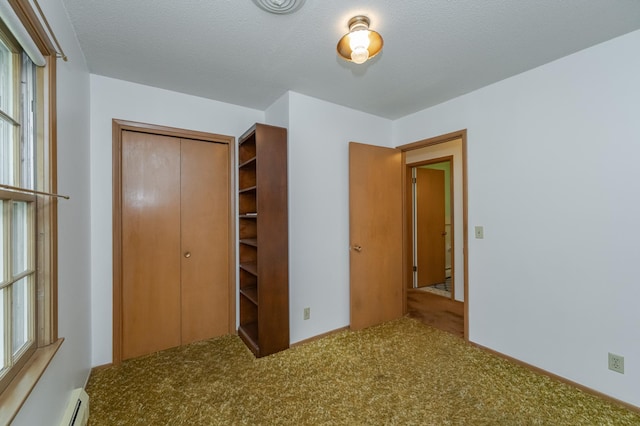 unfurnished bedroom with a textured ceiling, carpet, a baseboard heating unit, and a closet