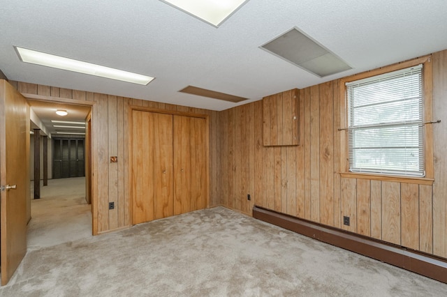 interior space with a baseboard radiator, wooden walls, a textured ceiling, and light carpet