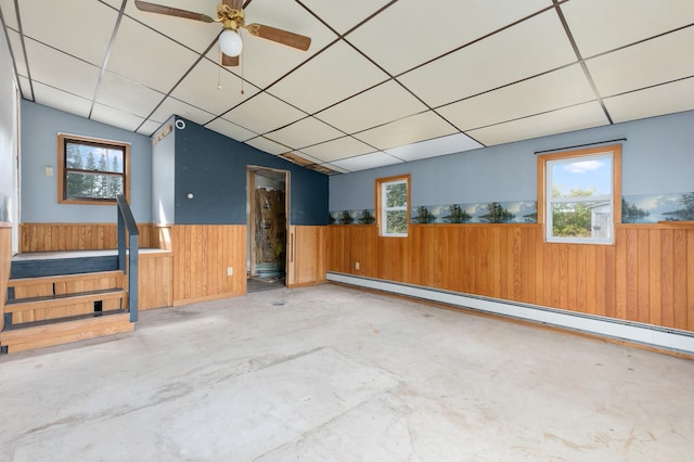 2135 24th Ave SW, Pine River Twp, MN 56474 - unfurnished room featuring a wainscoted wall, a baseboard heating unit, wood walls, unfinished concrete flooring, and healthy amount of natural light