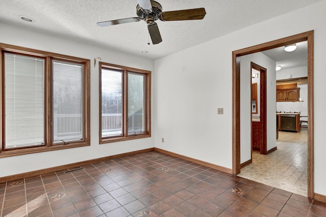 unfurnished room with ceiling fan, a textured ceiling, and dark tile patterned floors