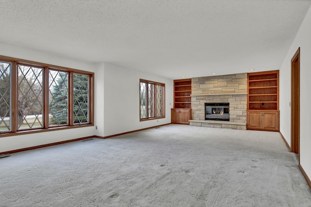 unfurnished living room featuring built in shelves, a fireplace, light carpet, and a textured ceiling