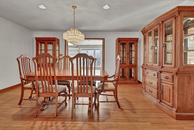 dining area with a textured ceiling, light hardwood / wood-style floors, and a chandelier