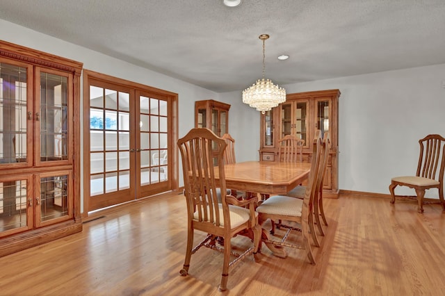 dining area featuring a chandelier, a textured ceiling, light wood-type flooring, and french doors