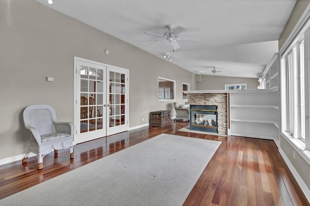 living room with french doors, wood-type flooring, vaulted ceiling, ceiling fan, and a fireplace