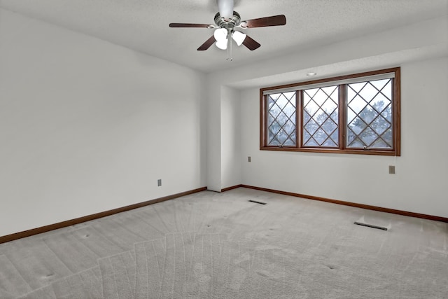 empty room with ceiling fan, light colored carpet, and a textured ceiling