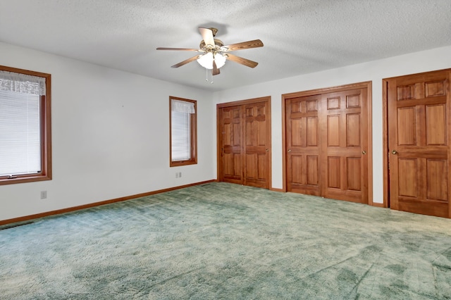 unfurnished bedroom with ceiling fan, carpet flooring, a textured ceiling, and two closets