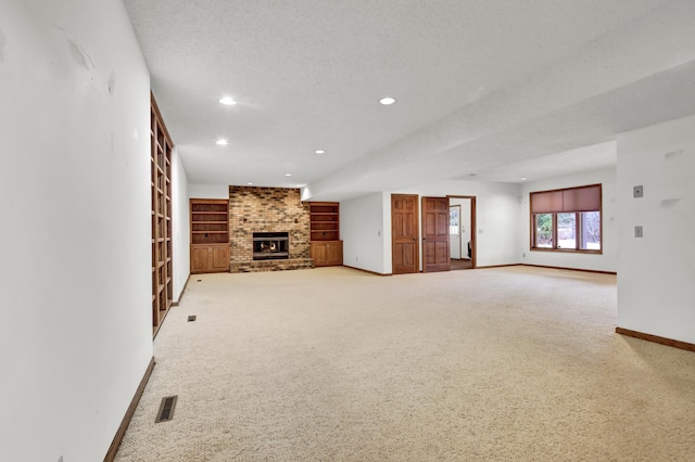 unfurnished living room featuring carpet, a fireplace, a textured ceiling, and built in shelves