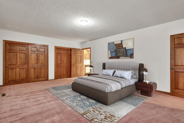 bedroom featuring a textured ceiling, light carpet, and two closets