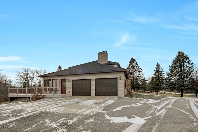 view of front of property featuring a deck, an attached garage, a chimney, and roof with shingles